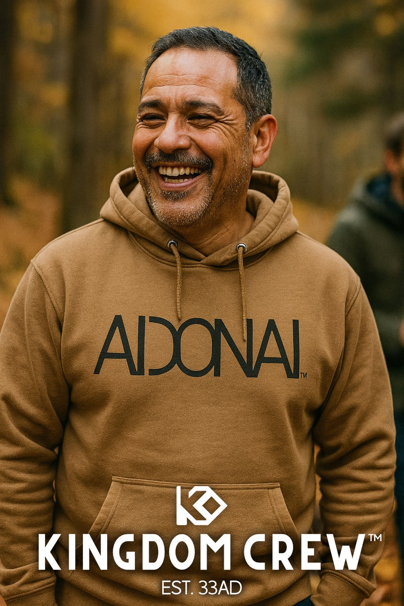 Man wearing a brown hoodie with 'AIDONAI' and 'Kingdom Crew' branding outdoors.