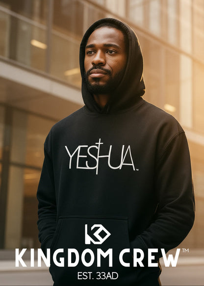 Man wearing a black hoodie with 'YESHUA' text, standing in front of a modern building.