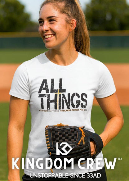 Person wearing a white t-shirt with 'All Things' text and a black and orange glove, standing on a baseball field.
