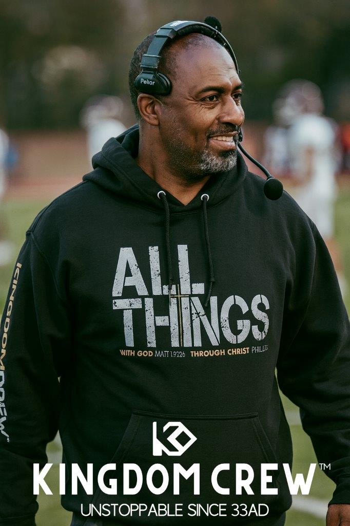 Man wearing a black hoodie with 'All Things' text and Kingdom Crew logo on a sports field.