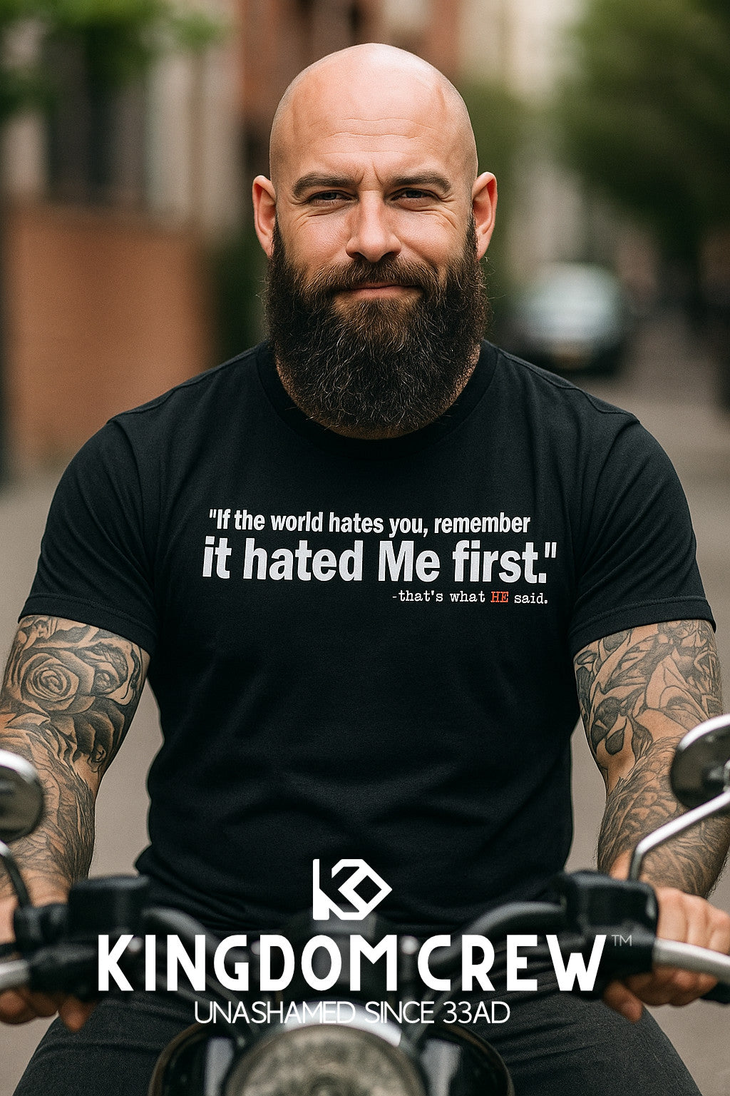 Man with tattoos and a beard wearing a black t-shirt with a quote, sitting on a motorcycle with 'Kingdom Crew' branding.